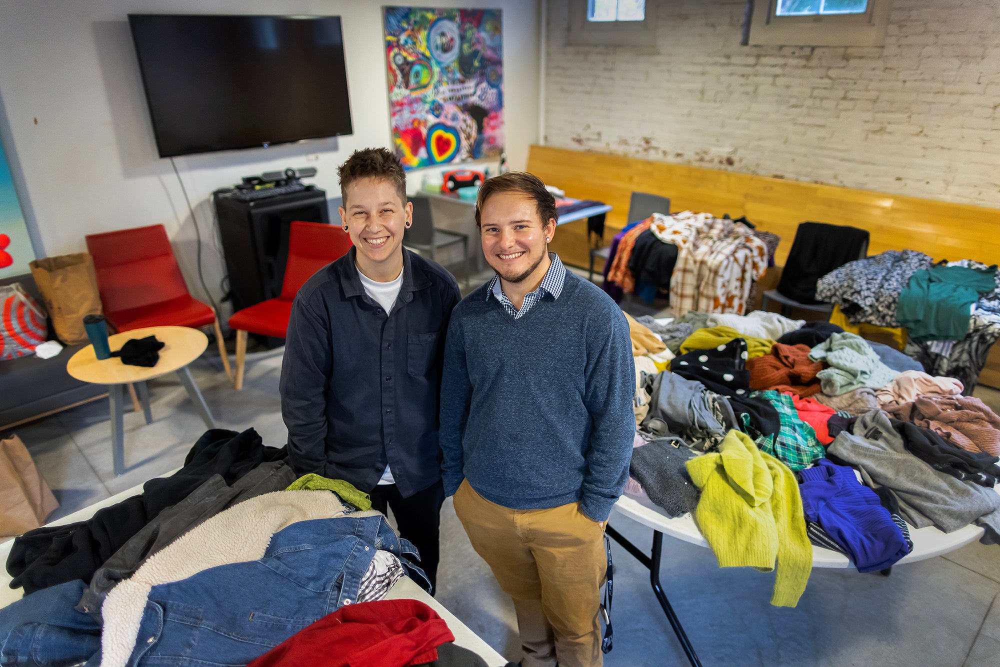 Two staffers stand in front of a pile of clothes on a large table.