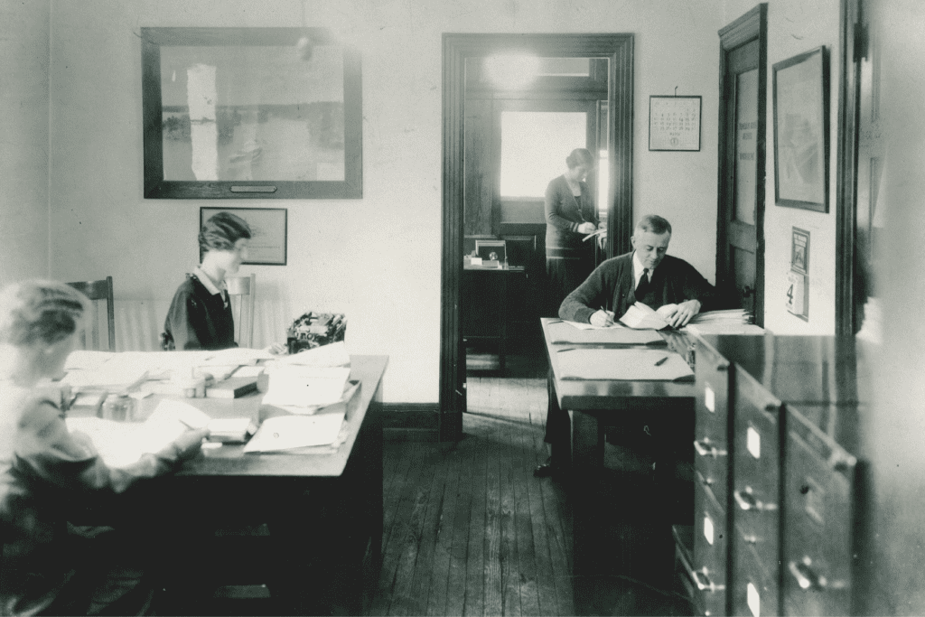 A black and white photo captures individuals diligently working in an office.