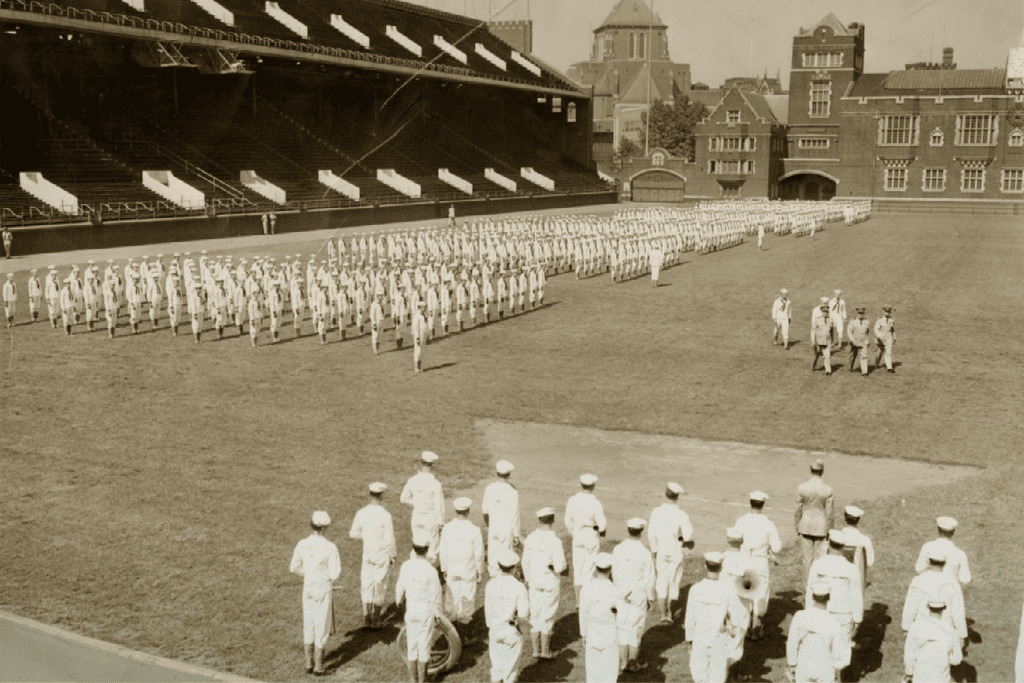 Rows of navy students in white uniforms fill Franklin Field in this sepia tone photo.