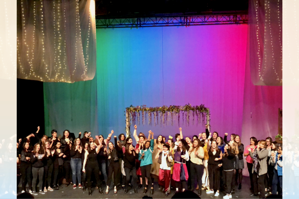 Dozens of students are cheering on stage in front of a colorful backdrop.